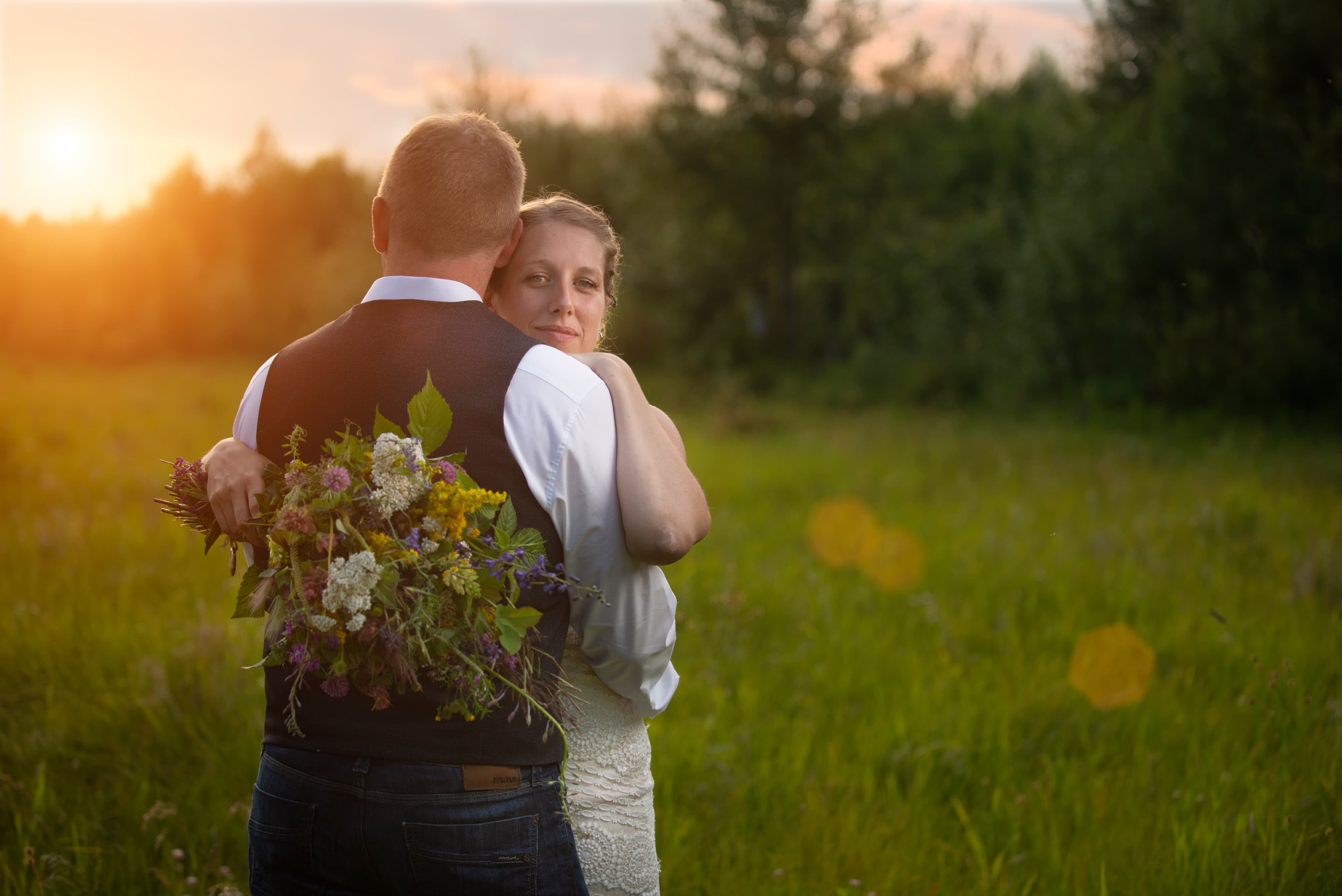 Newlywed couple embracing in a field at sunset